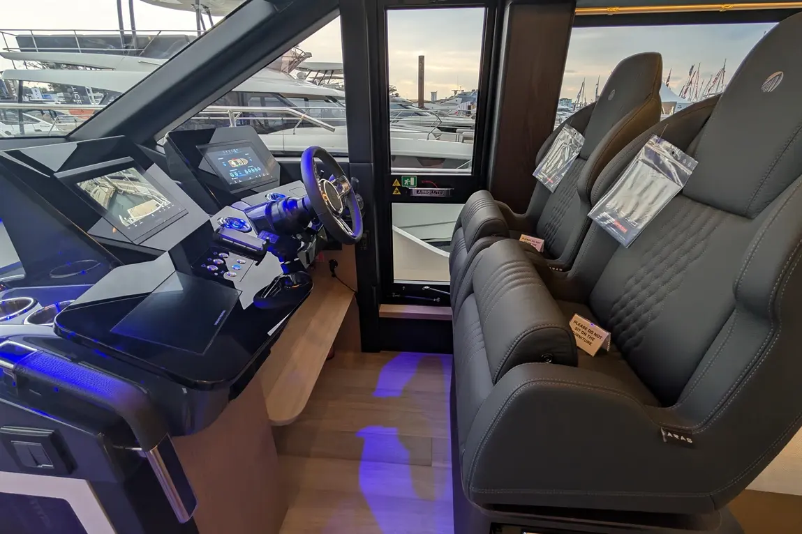 Luxury yacht cockpit featuring advanced navigation screens, a steering wheel, and plush seating with safety instructions visible.